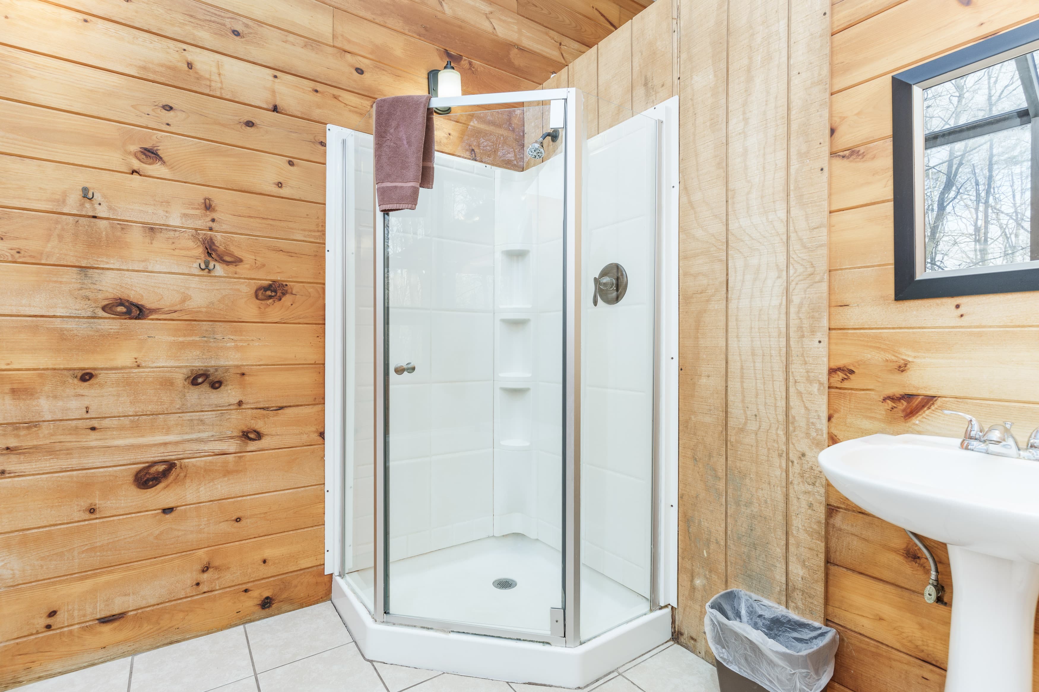 A clean shower enclosure in a wooden bathroom featuring a sink and a window.