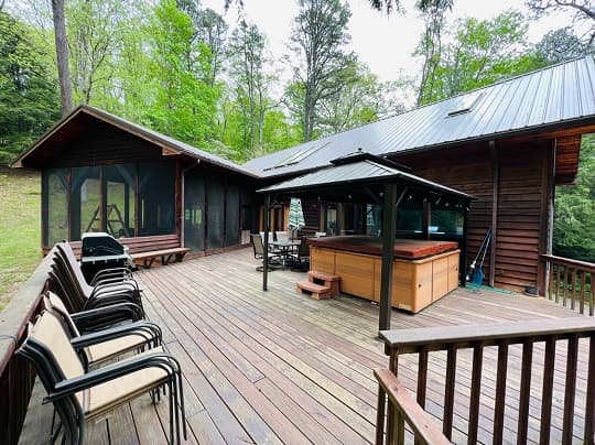 Wooden deck with seating, a hot tub, and a cabin surrounded by trees.