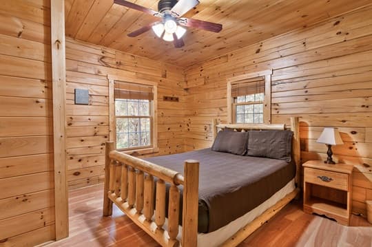 Cozy wooden bedroom featuring a log bed, two windows, and a bedside lamp.