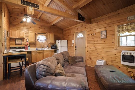 Cozy wooden cabin interior featuring a sofa, kitchenette, and door with a welcoming atmosphere.