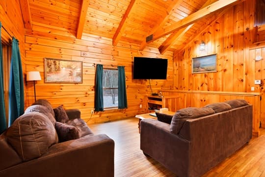 Cozy cabin interior with wooden walls, comfortable sofas, and a large window.