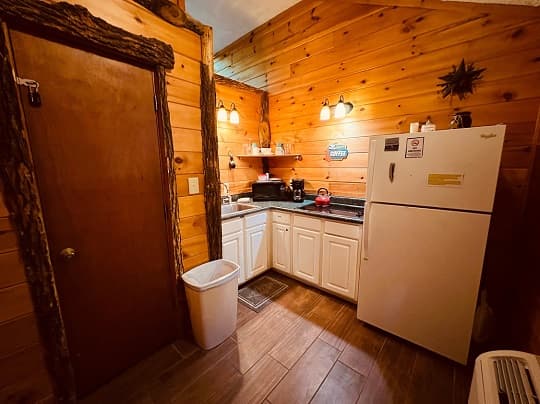 A cozy kitchen with wooden walls, featuring a refrigerator, sink, and countertop appliances.