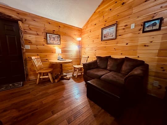 Cozy cabin living area with wooden walls, a brown couch, a small table, and warm lighting.
