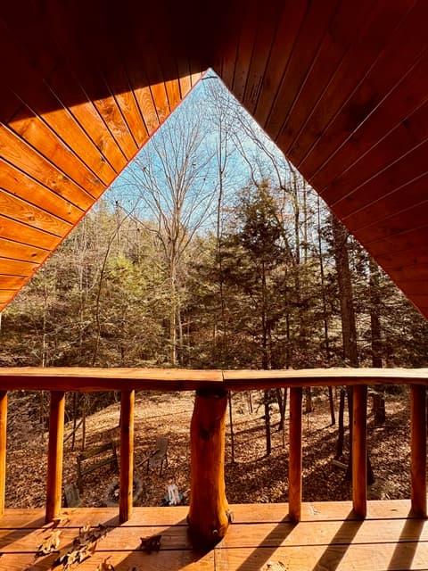View from a wooden balcony framing a serene forest landscape under a clear blue sky.