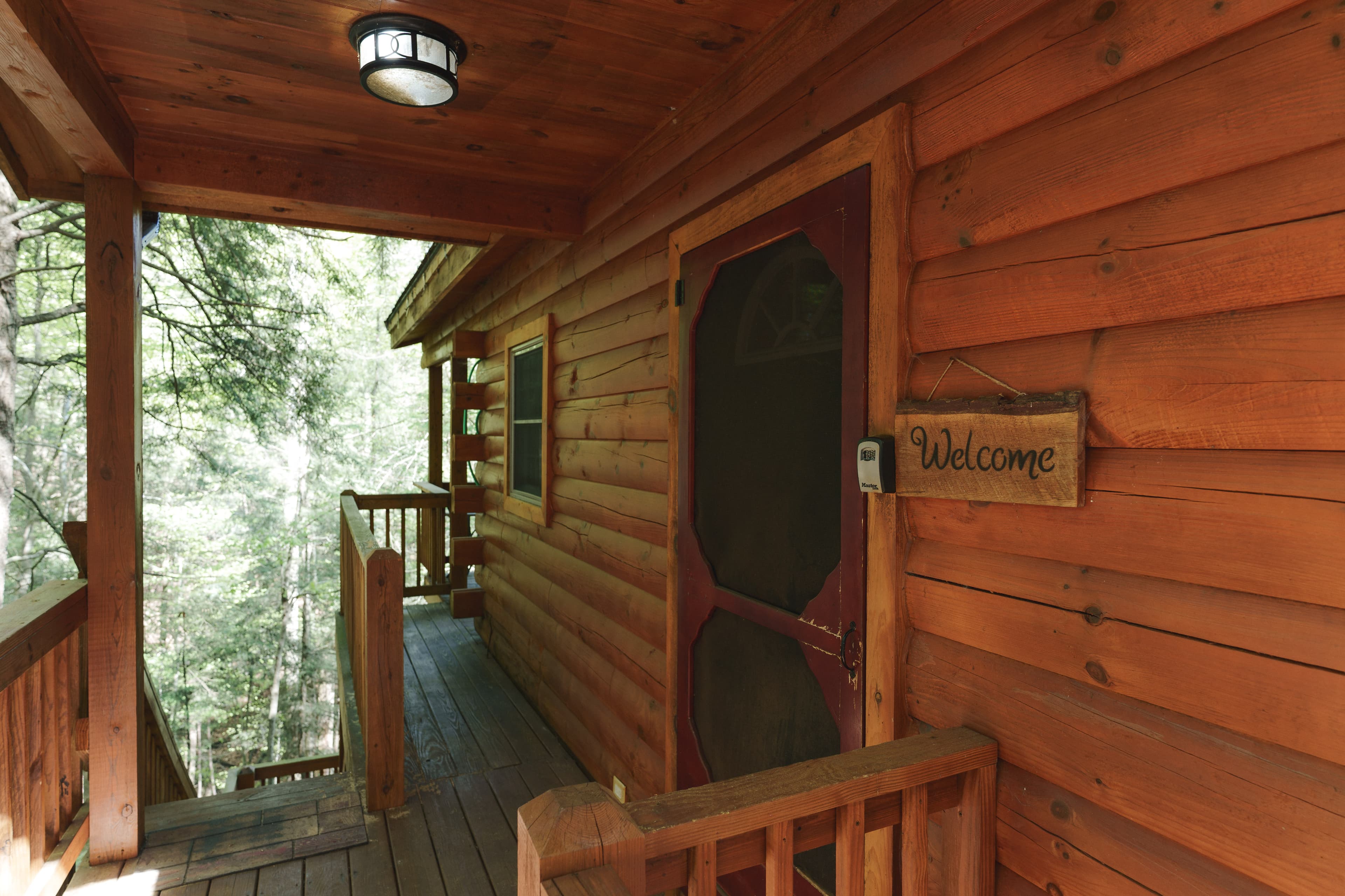 A wooden porch of a log cabin with a "Welcome" sign hanging beside the door.