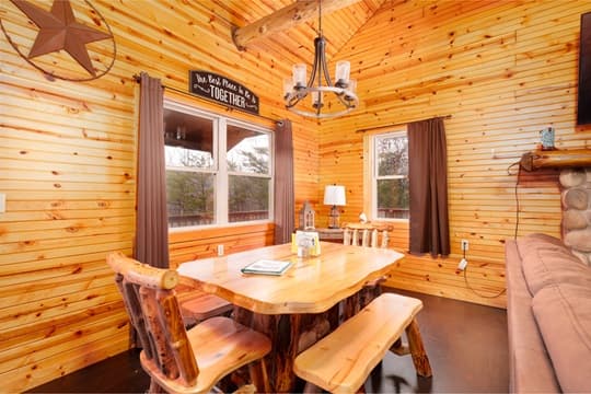 A cozy wooden dining area featuring a rustic table, benches, and large windows with curtains.