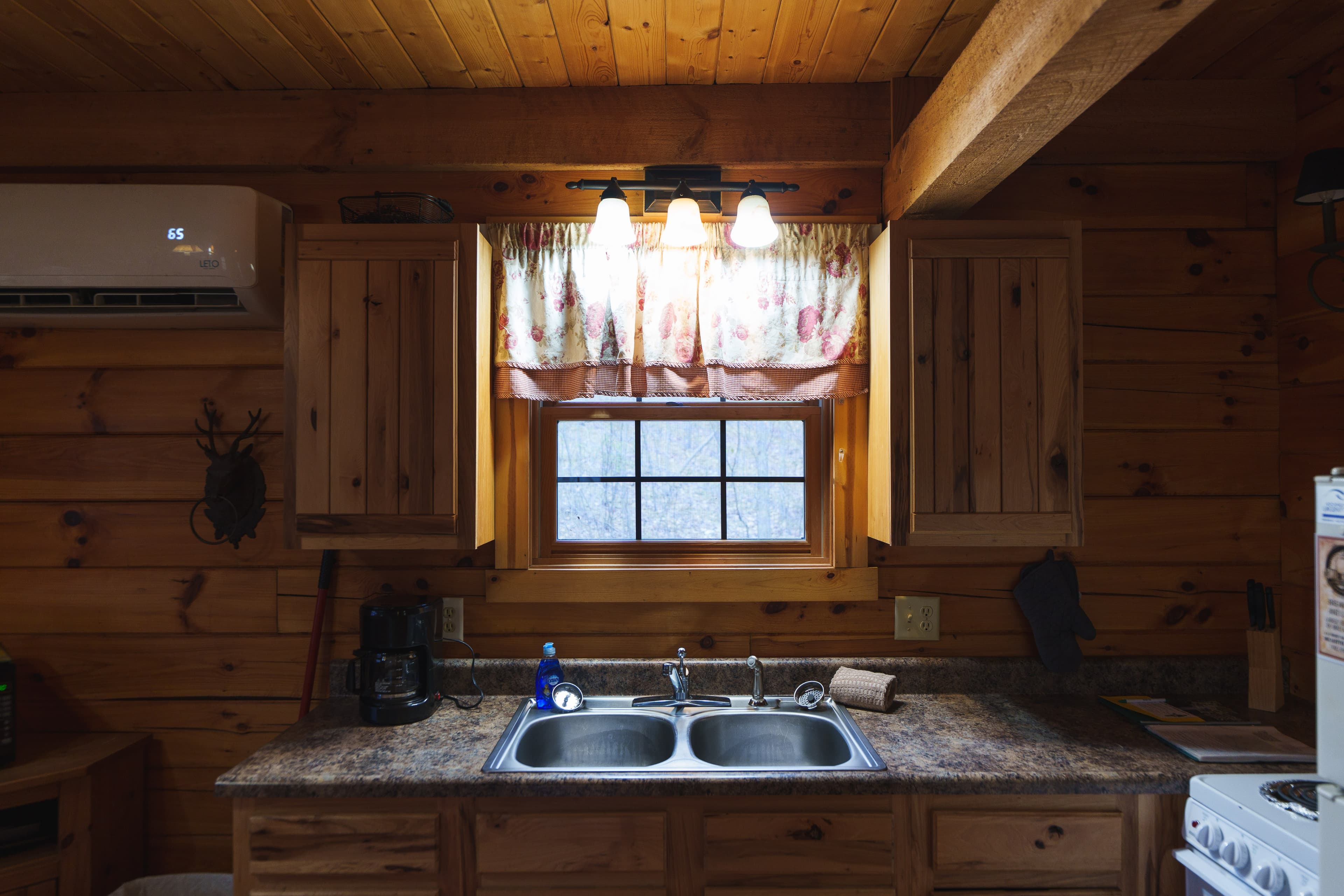 Cozy wooden kitchen with a double sink, window, and floral curtain.