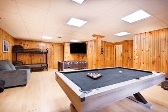 A cozy game room featuring a pool table, a couch, and wooden paneling.