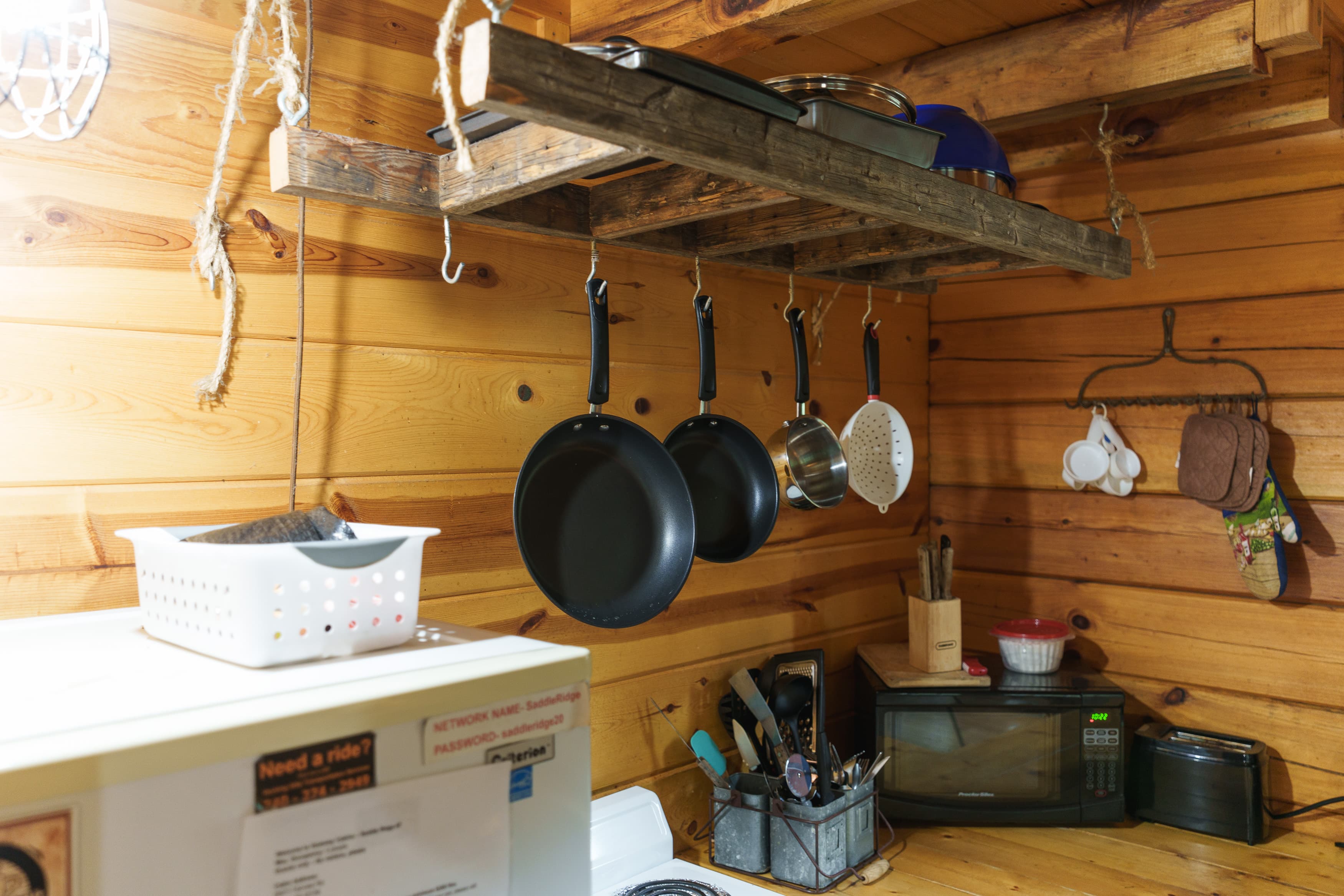 A cozy wooden kitchen with hanging pots, a microwave, and various utensils.