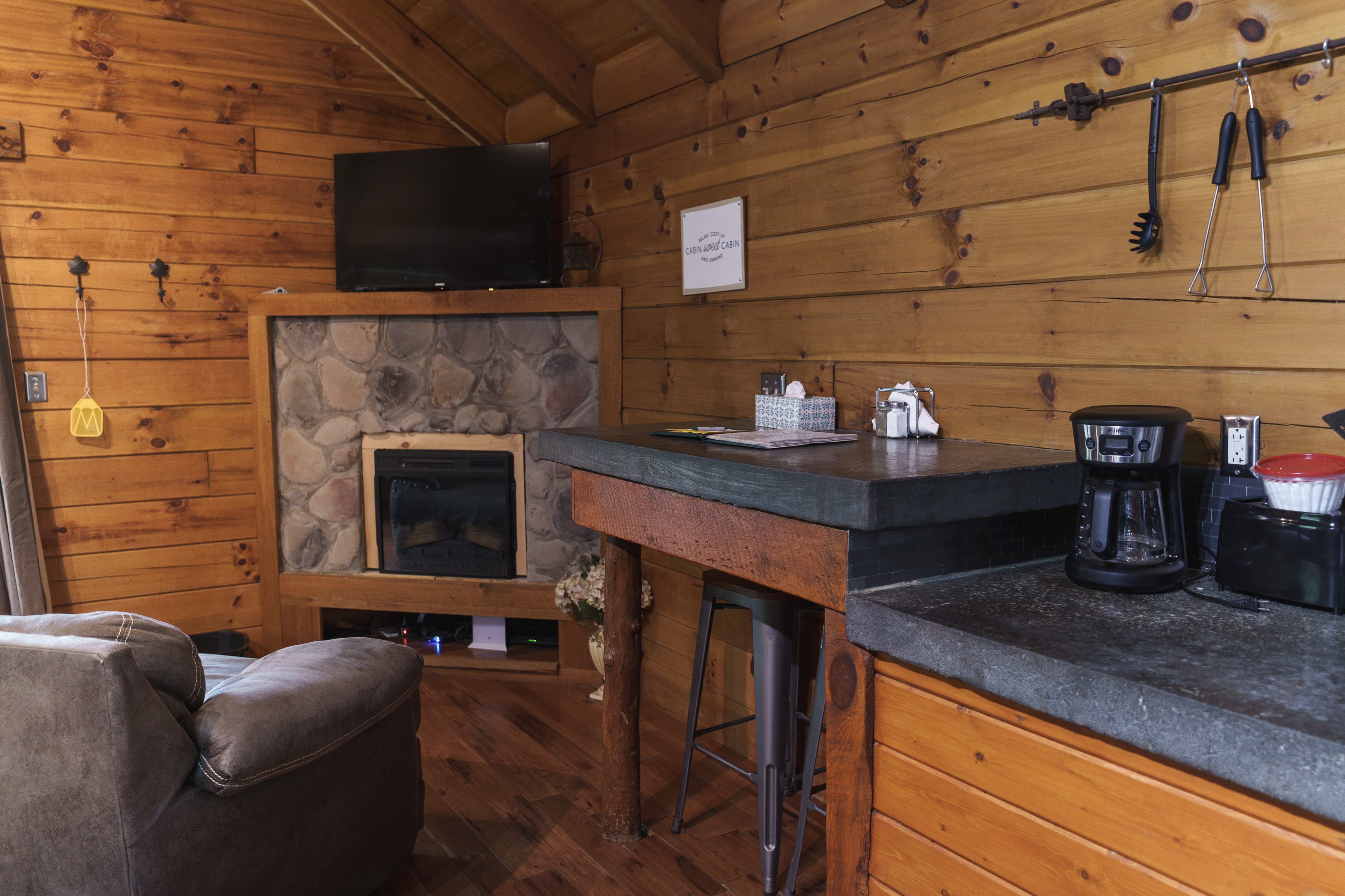 Cozy interior of a cabin featuring wooden walls, a fireplace, a coffee maker, and a comfortable chair.