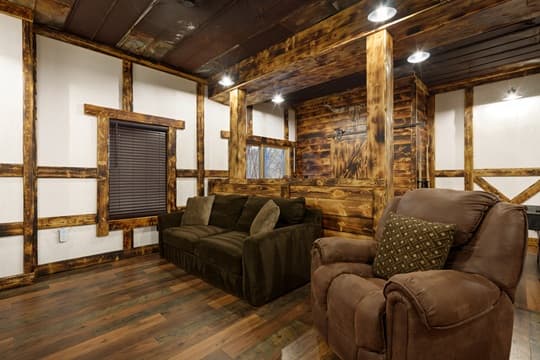 A cozy living room with rustic wooden walls, a dark sofa, and a comfortable recliner.