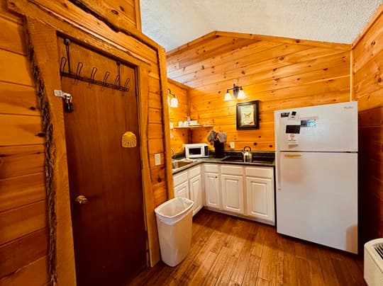 A cozy wooden kitchen featuring white cabinets, a refrigerator, and rustic decor.