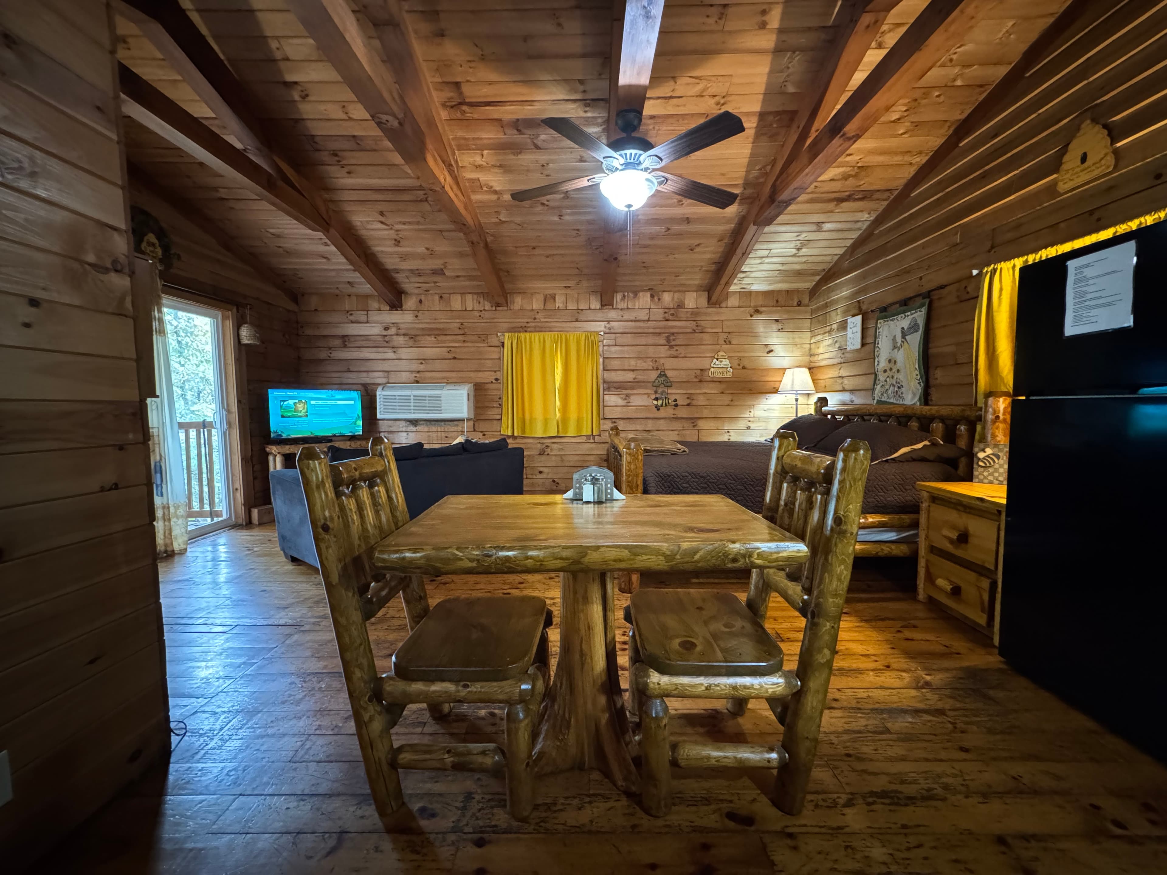 Cozy wooden cabin interior featuring a dining table, two chairs, a small living area, and a kitchenette.