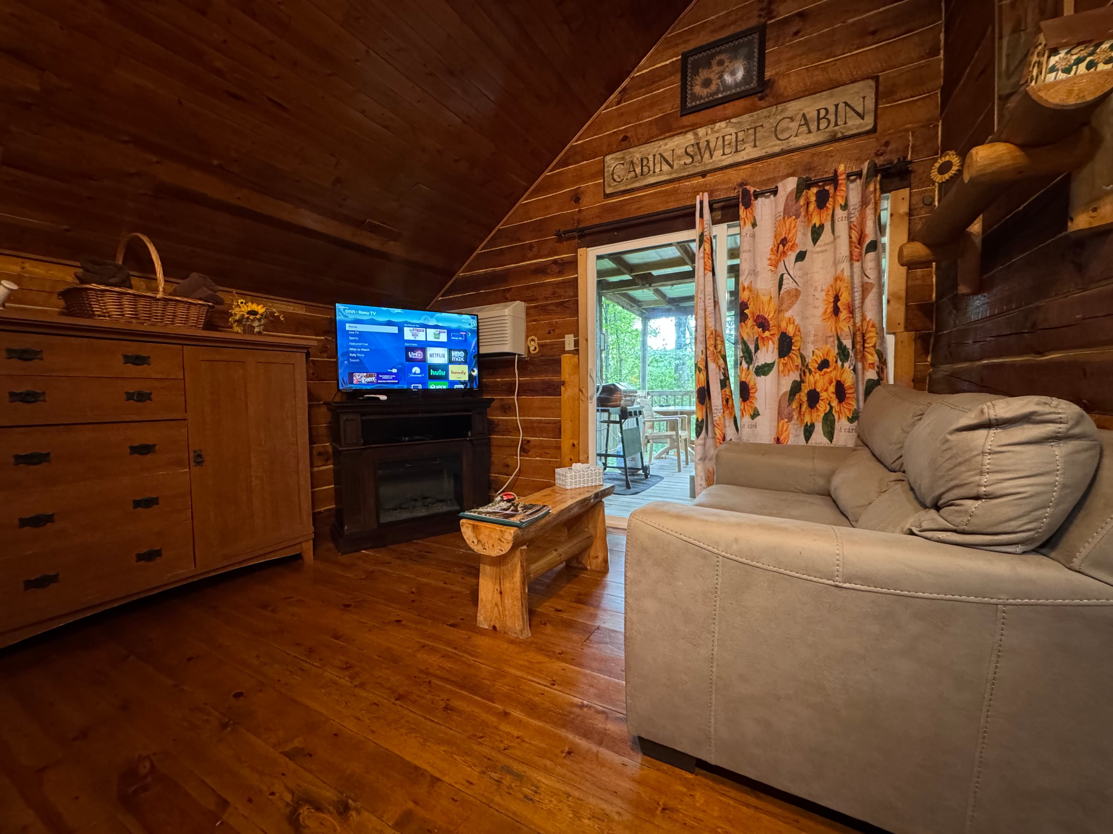 Cozy cabin interior featuring a TV, wooden furniture, and floral curtains.
