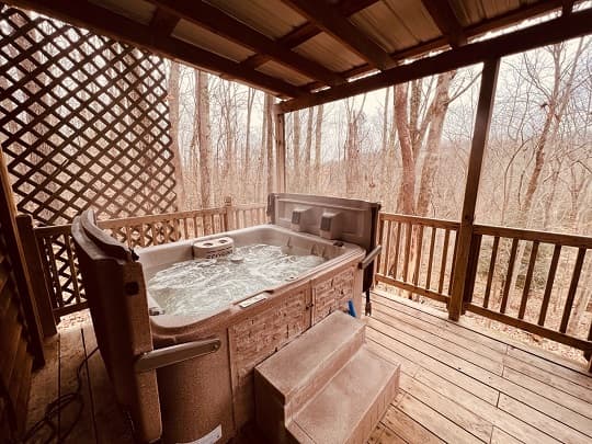 A hot tub on a wooden deck surrounded by bare trees.