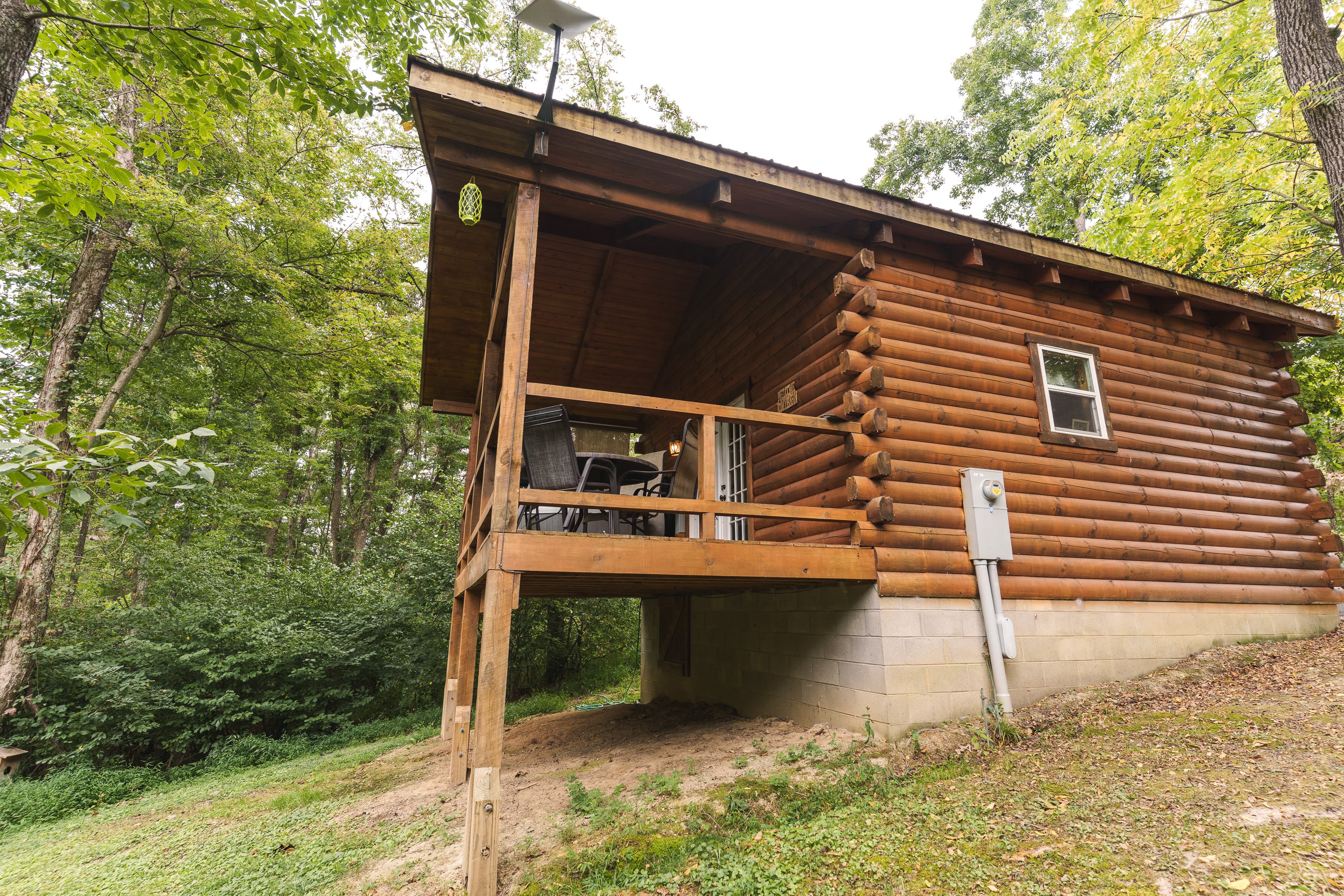 A rustic log cabin with a small porch surrounded by trees.