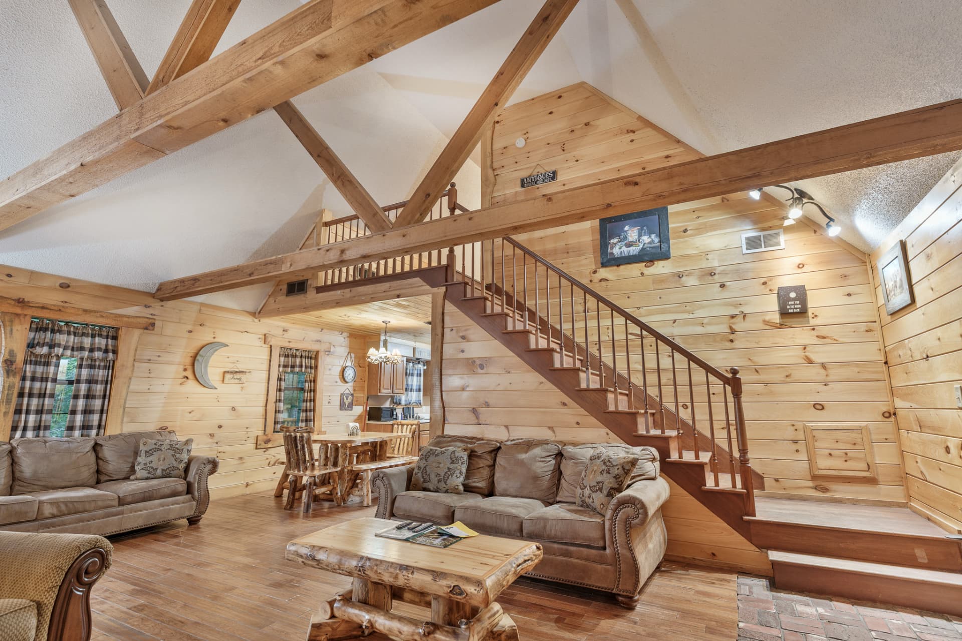 A cozy wooden interior featuring a living area with sofas, a dining table, and a staircase.