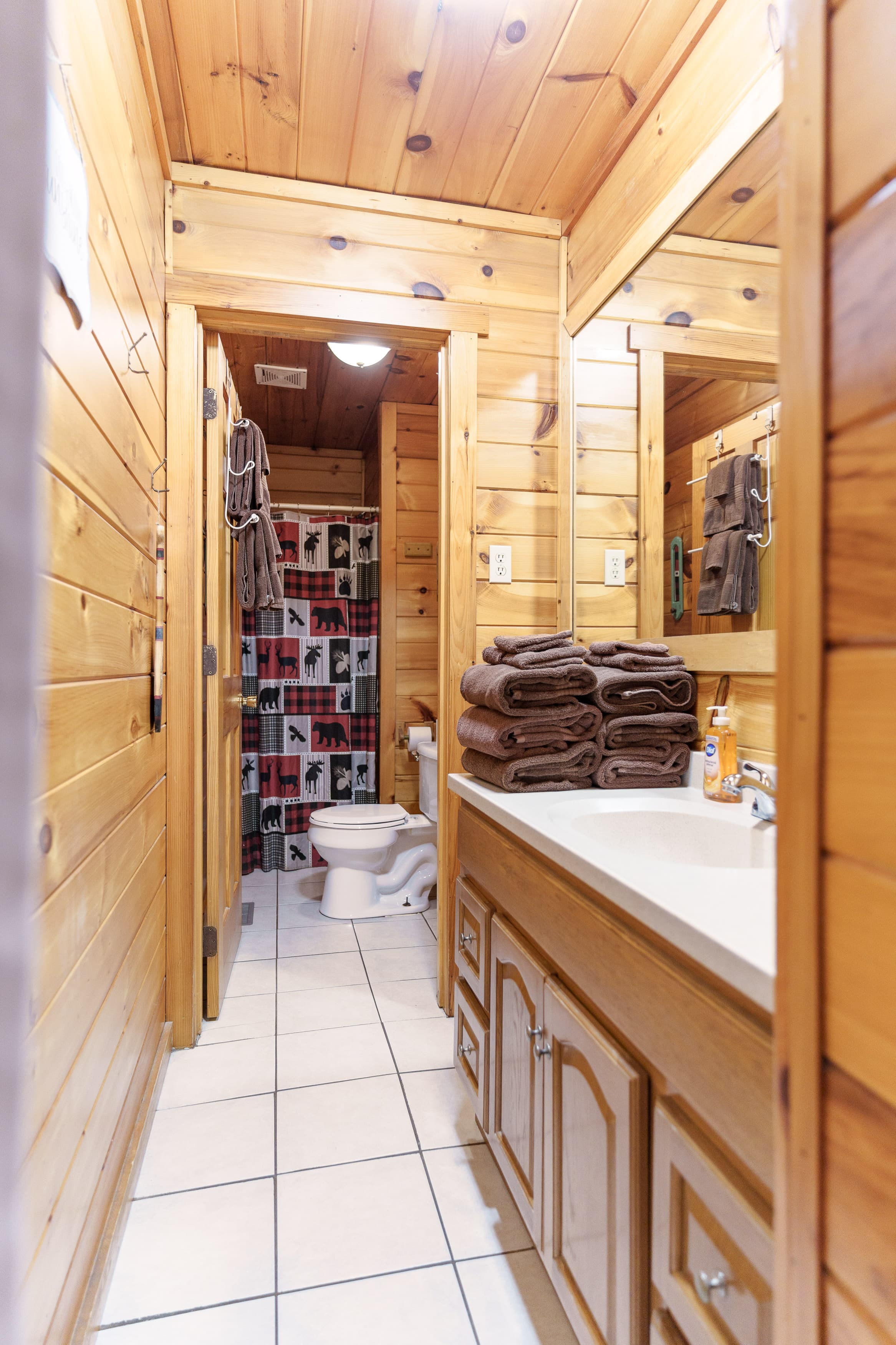 A cozy wooden bathroom with stacked towels, a sink, and a patterned shower curtain.