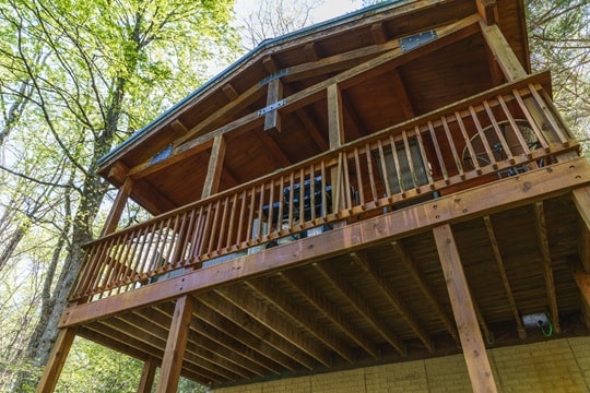 A wooden cabin with a balcony overlooking a forested area.