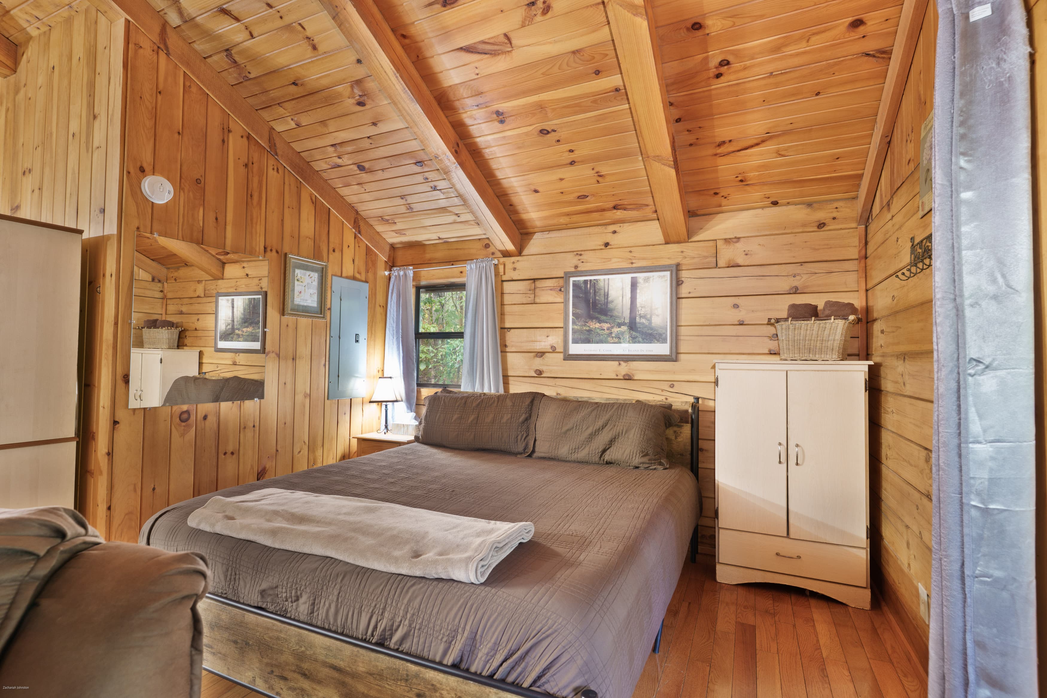Cozy wooden bedroom featuring a double bed, lamp, and rustic decor.