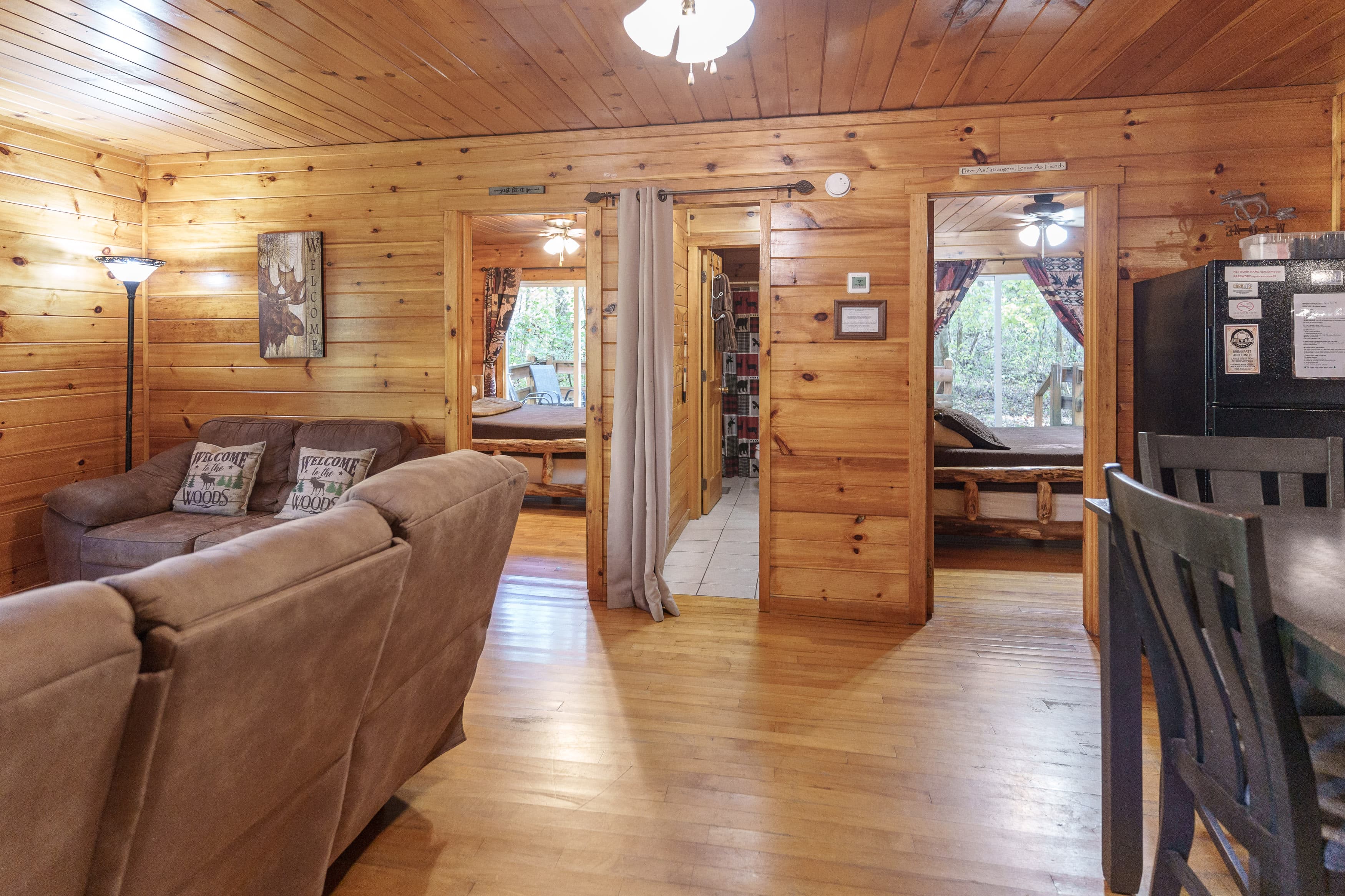 Cozy wooden interior of a cabin featuring a living area with a sofa, dining table, and doorways to other rooms.