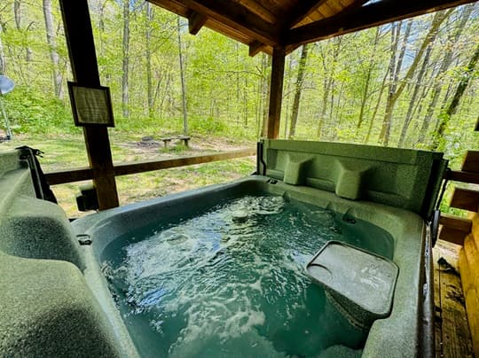 A bubbling hot tub surrounded by lush greenery and a wooden shelter.