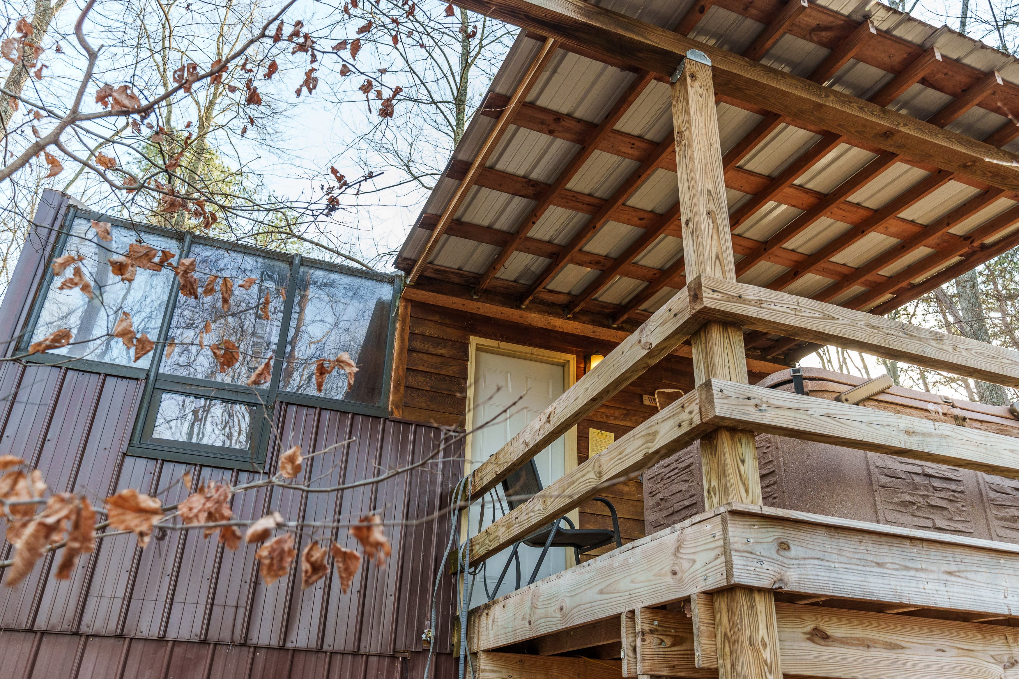 A wooden deck leads to the entrance of a rustic cabin surrounded by trees.