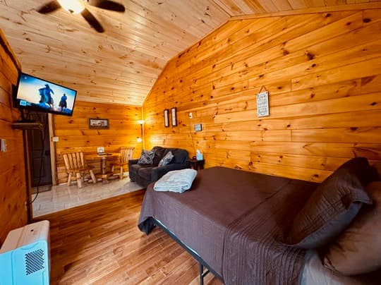 Cozy cabin interior featuring a wooden design, a bed, seating area, and a TV.