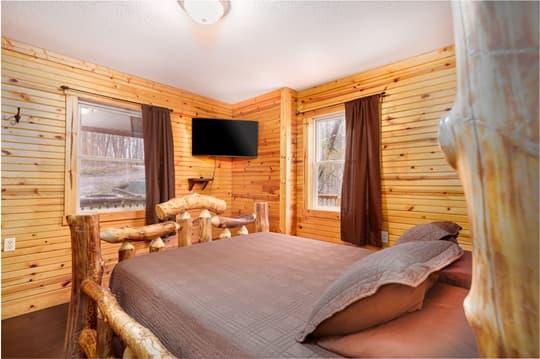 Cozy cabin bedroom with wooden walls, a bed, and a TV on the wall.