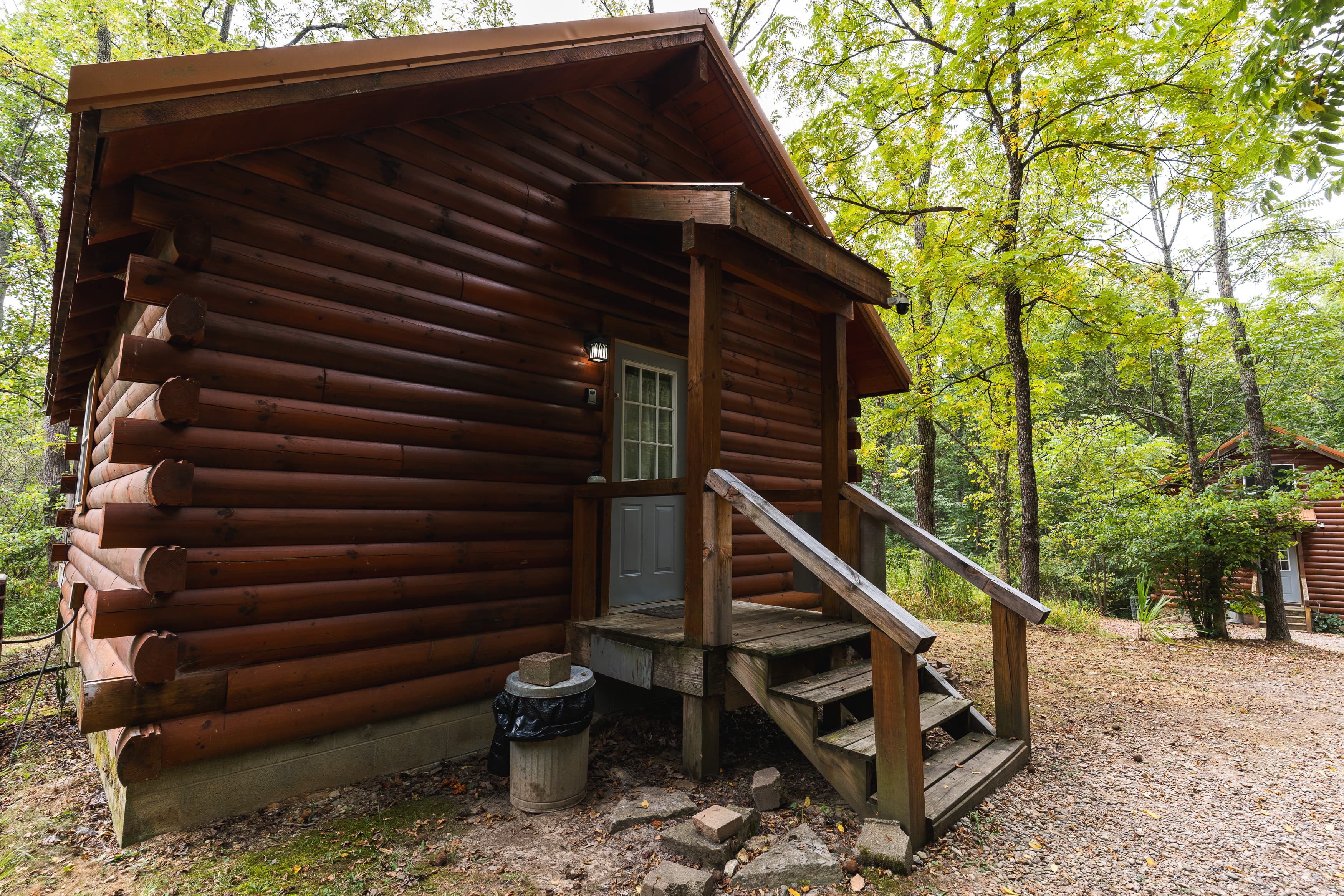 A small log cabin with a front porch surrounded by trees.