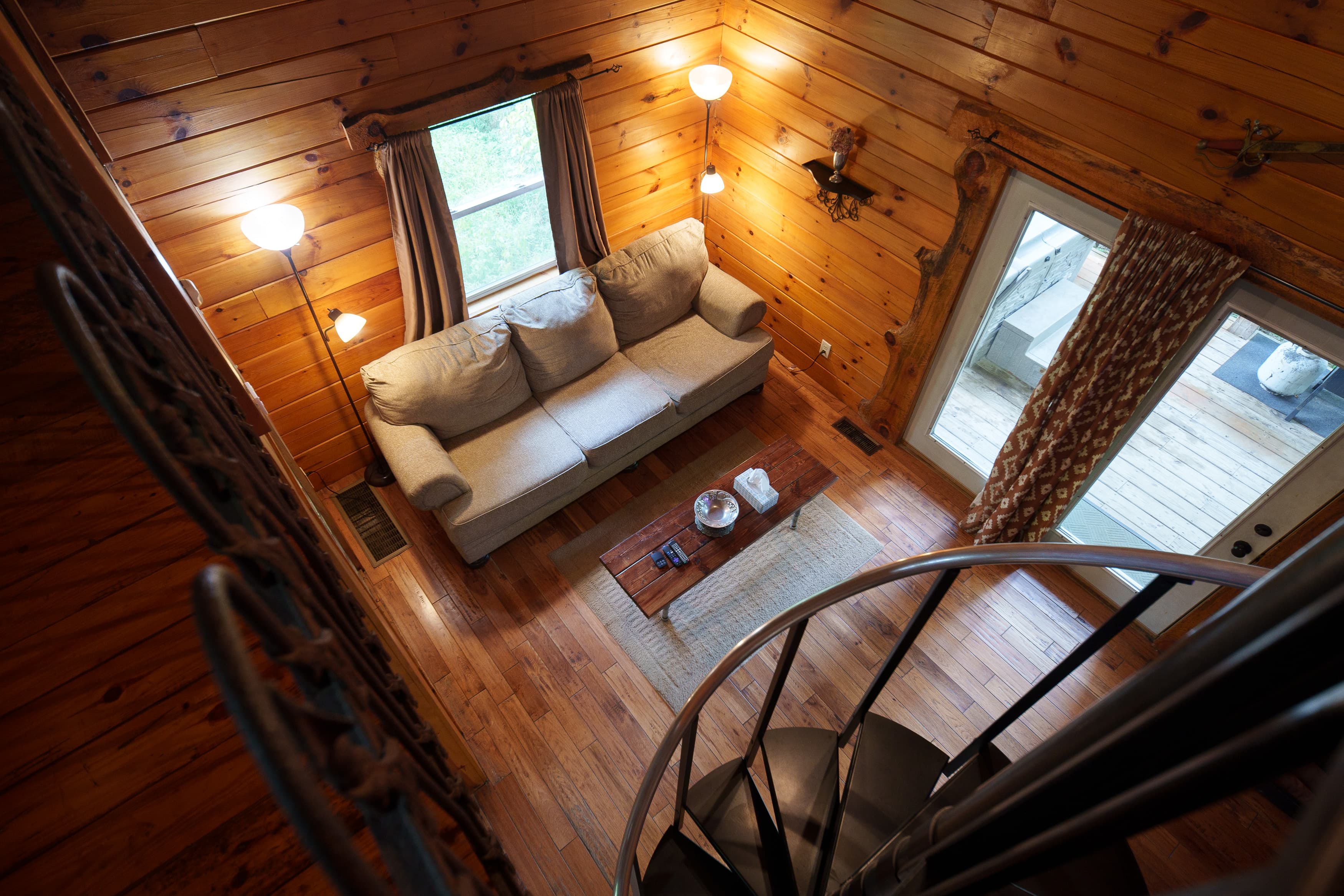 Aerial view of a cozy living room with wooden walls, a sofa, and a spiral staircase.