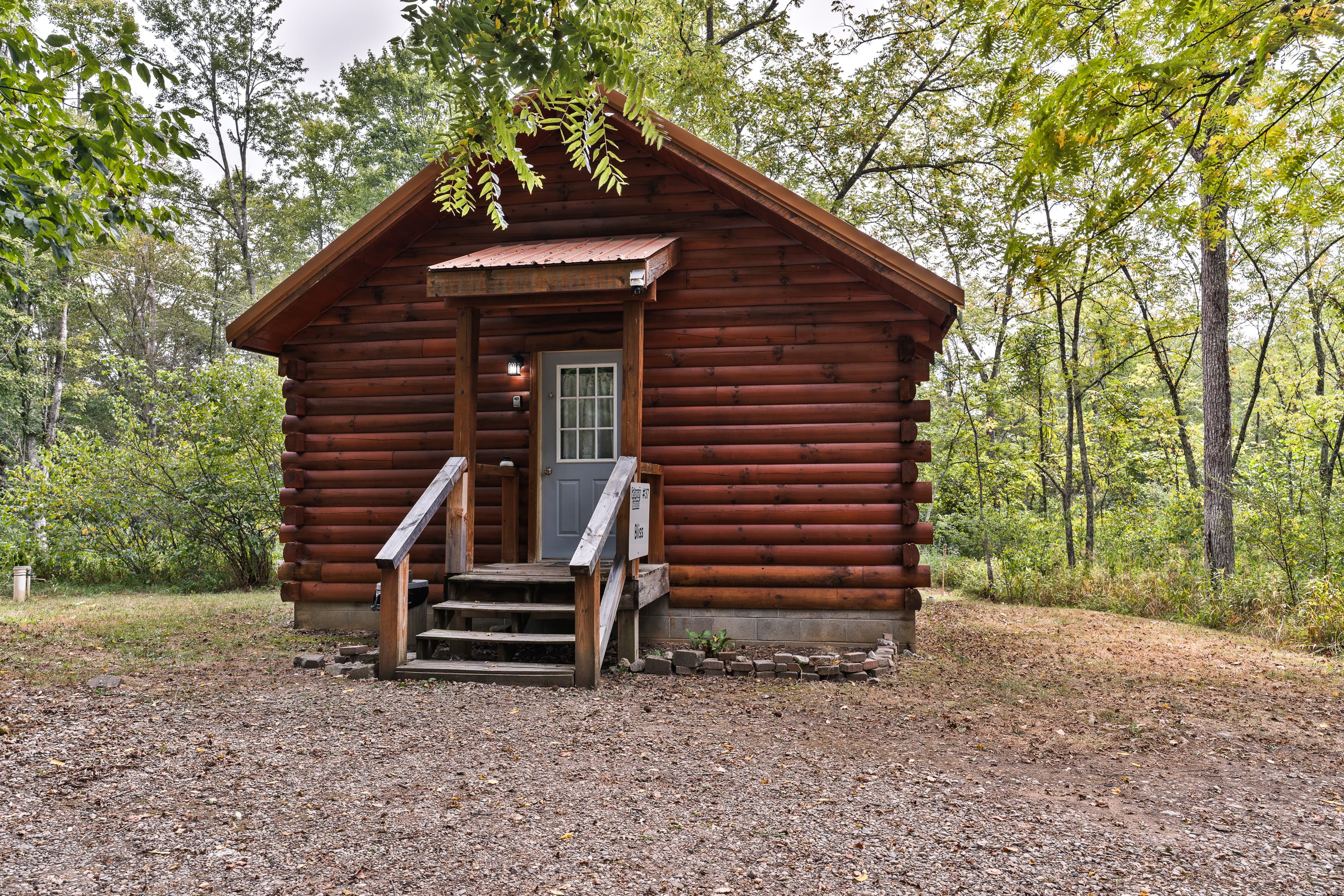A rustic log cabin with a front porch nestled among trees.