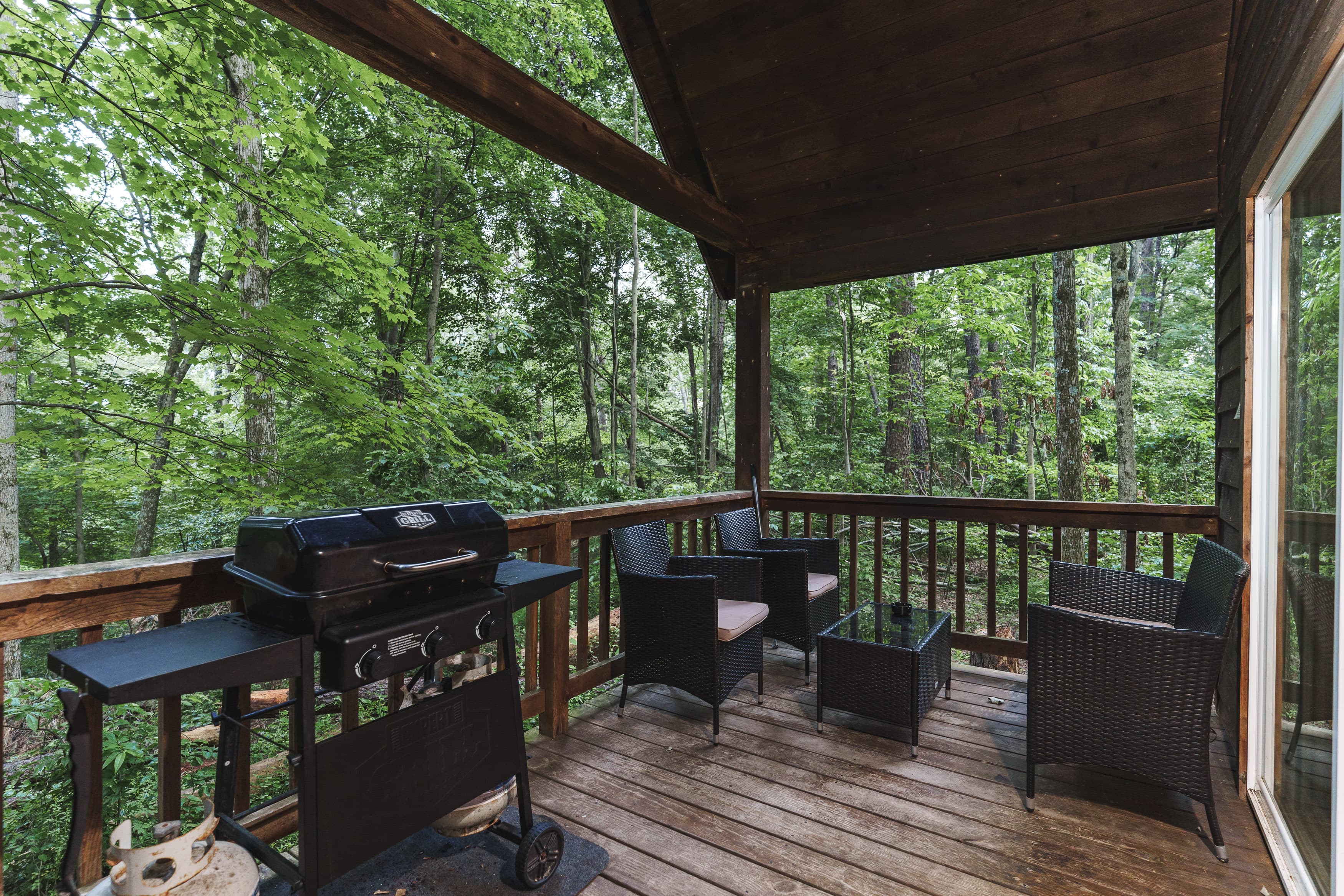 A wooden deck with a grill and seating area overlooks a lush, green forest.