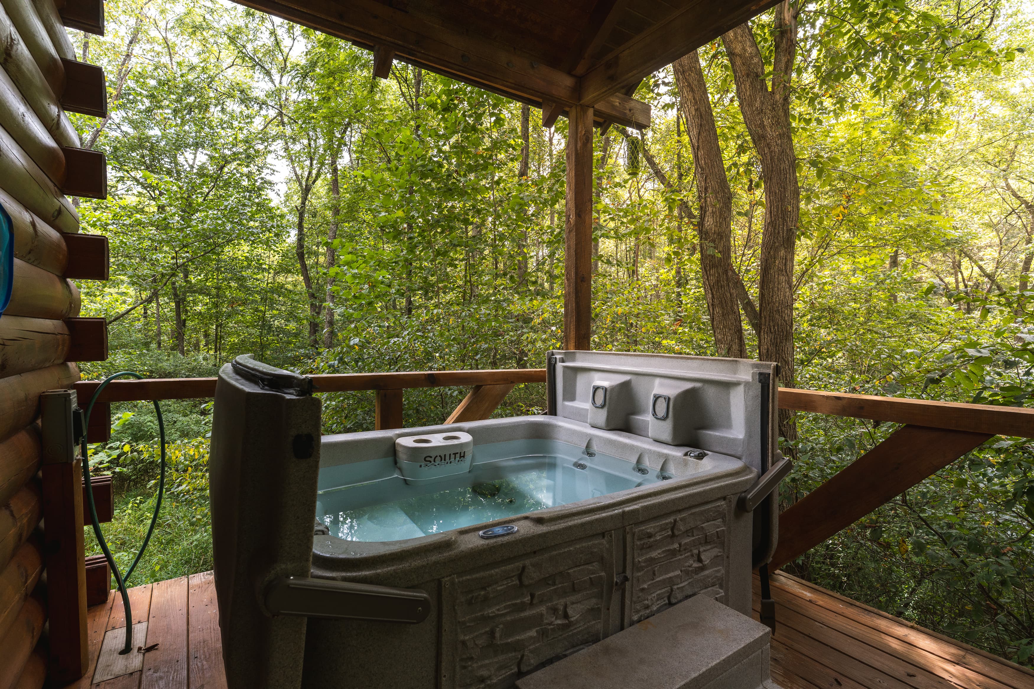 A hot tub on a wooden deck overlooking a lush forest.