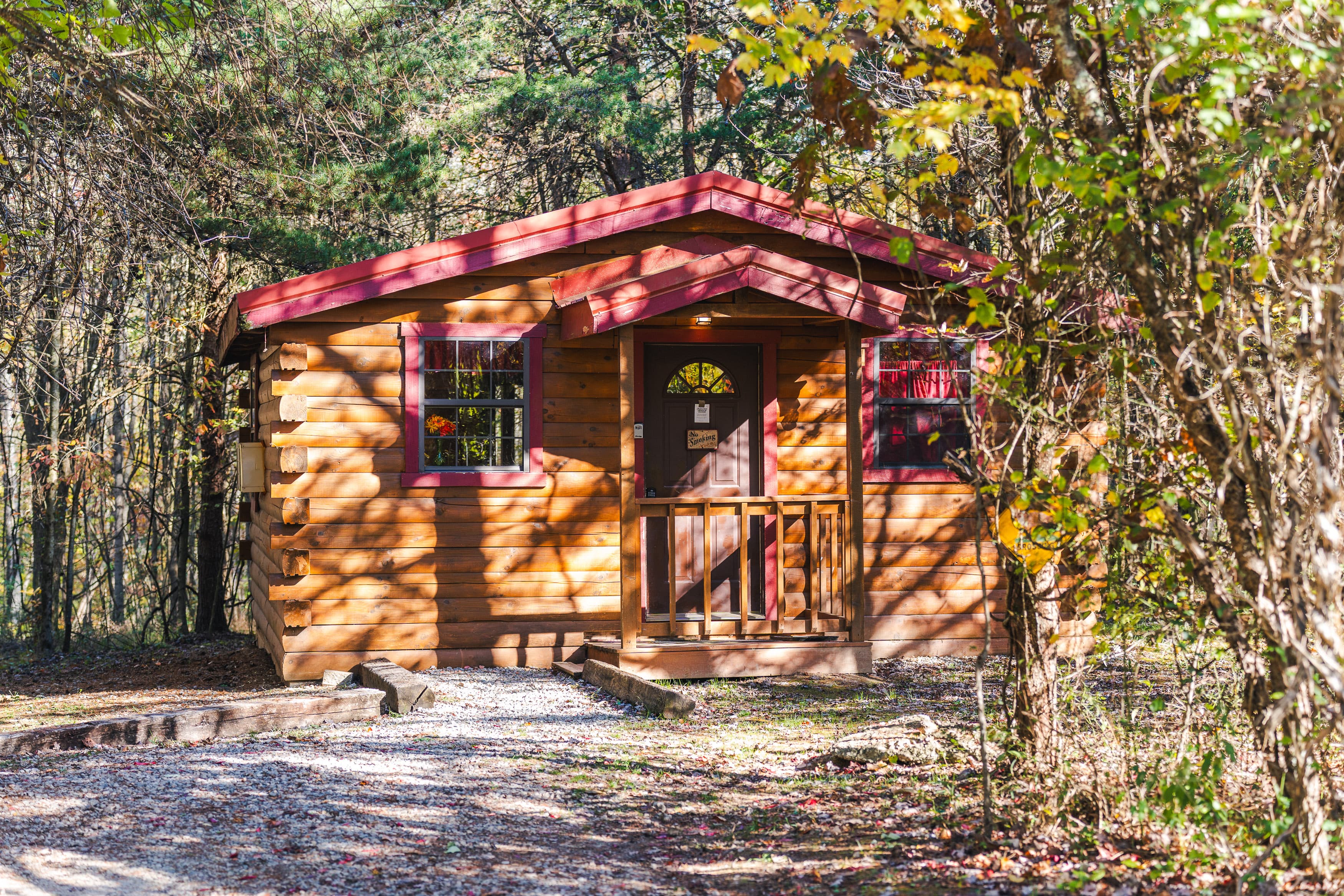 A small wooden cabin with a red roof surrounded by trees.