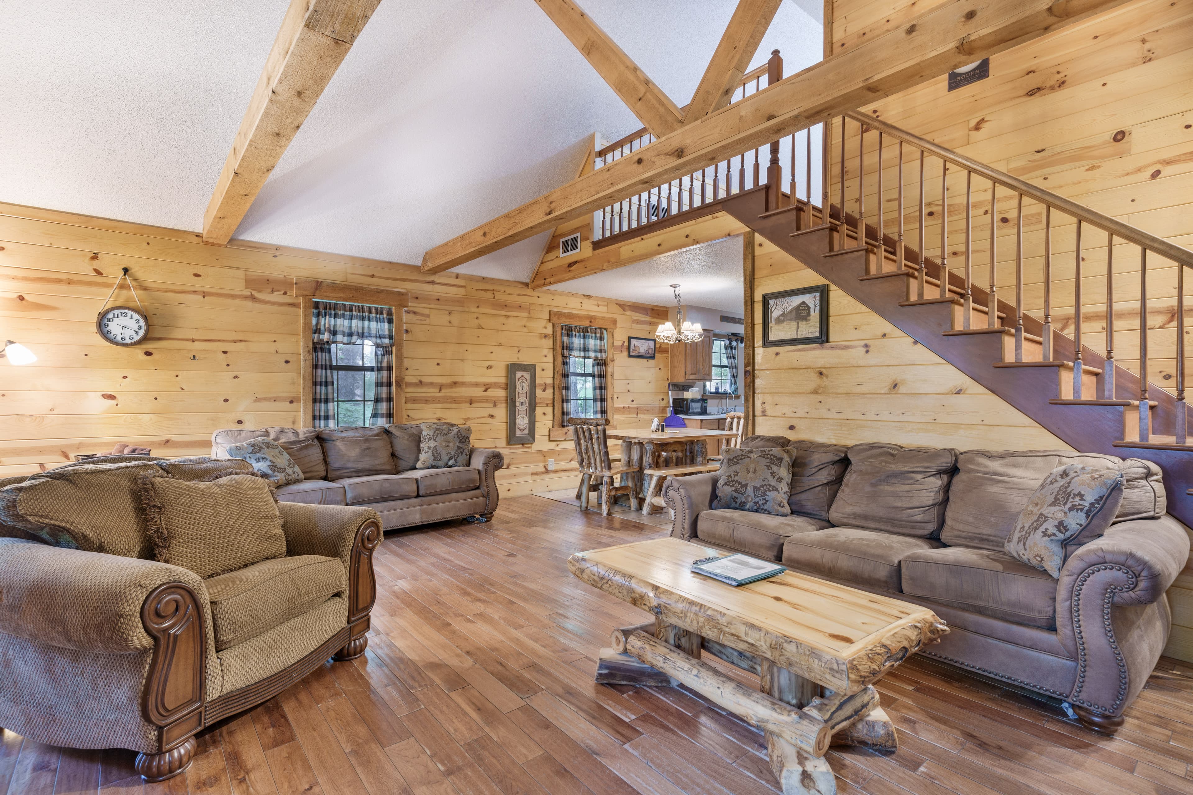 A cozy, wooden interior living room featuring comfortable sofas, a wooden coffee table, and a staircase leading to the upper level.