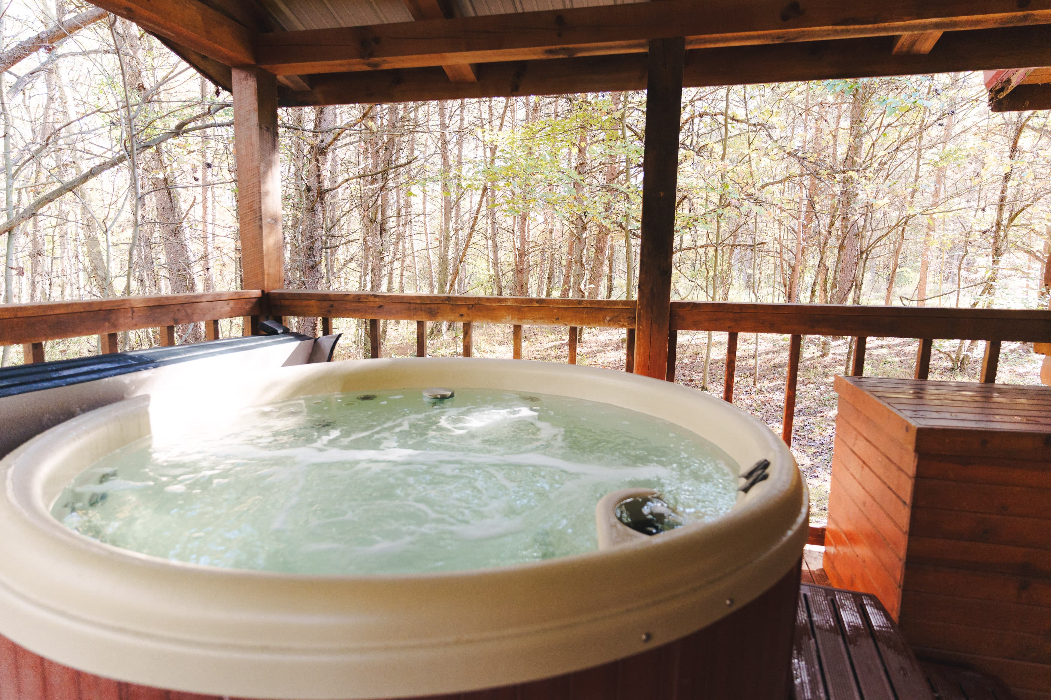 A hot tub with bubbling water on a wooden porch surrounded by trees.