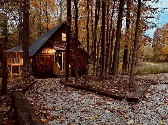A cozy cabin surrounded by autumn foliage and gravel pathways.