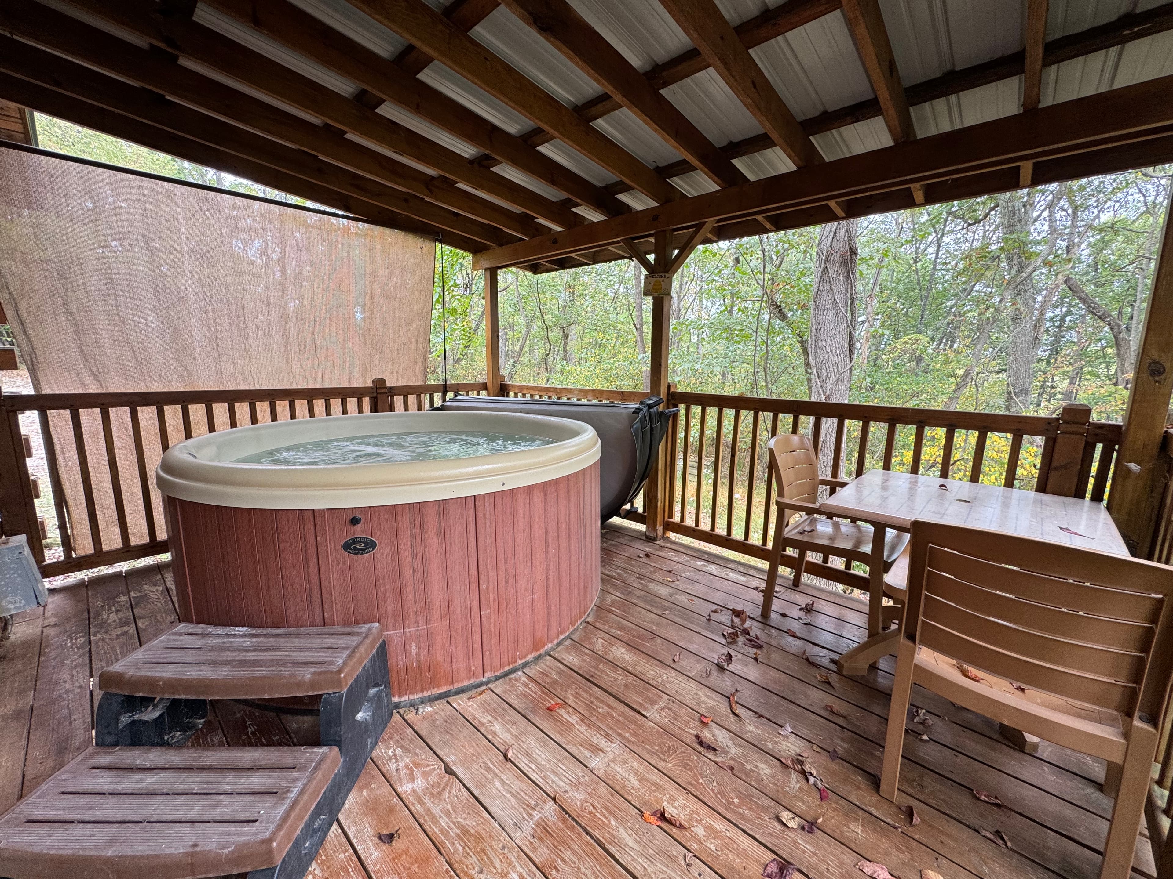 A covered porch features a hot tub, wooden seating, and views of a forest.