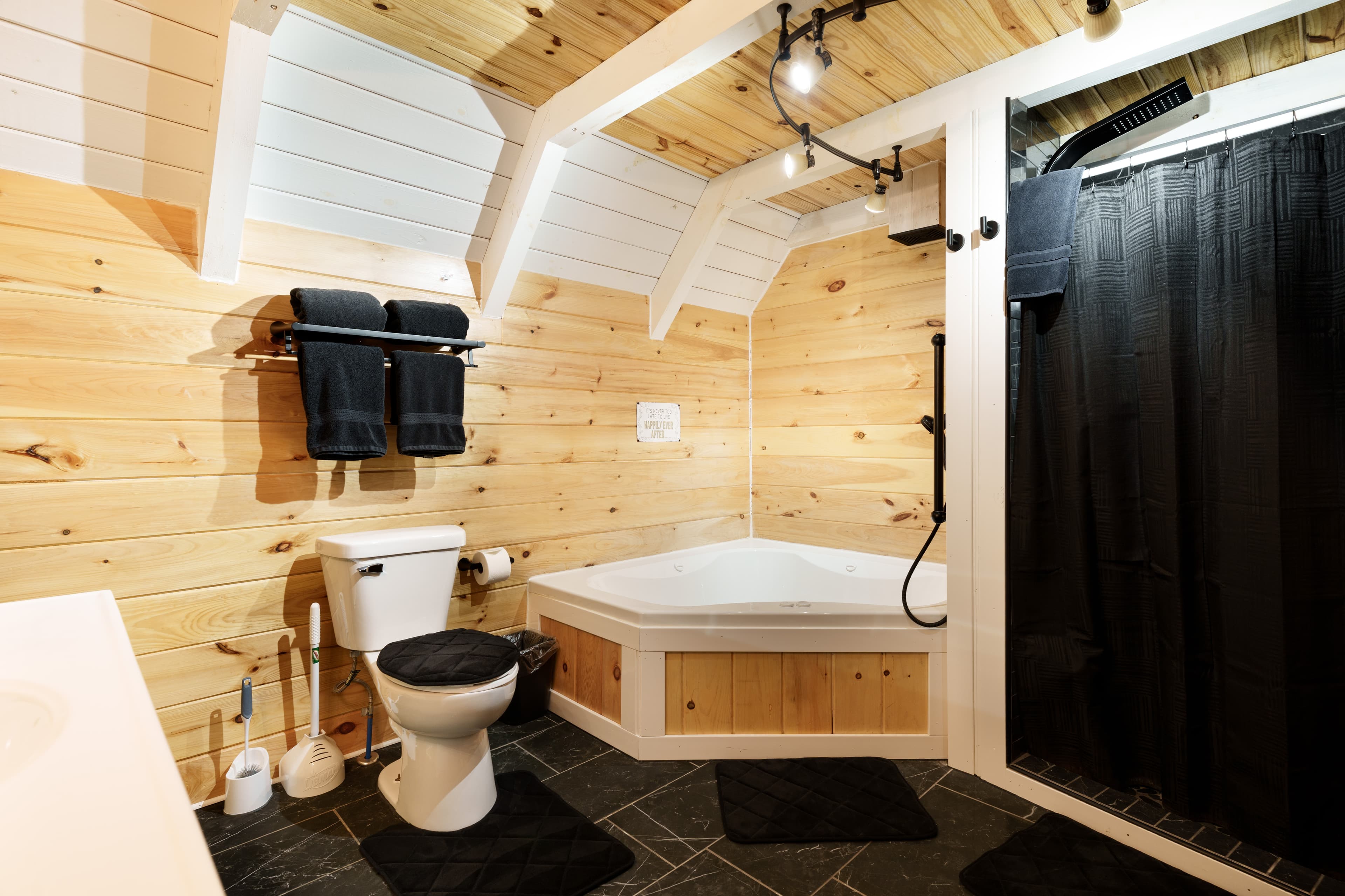 A modern bathroom featuring a wooden interior, a shower area, a bathtub, and black towels.