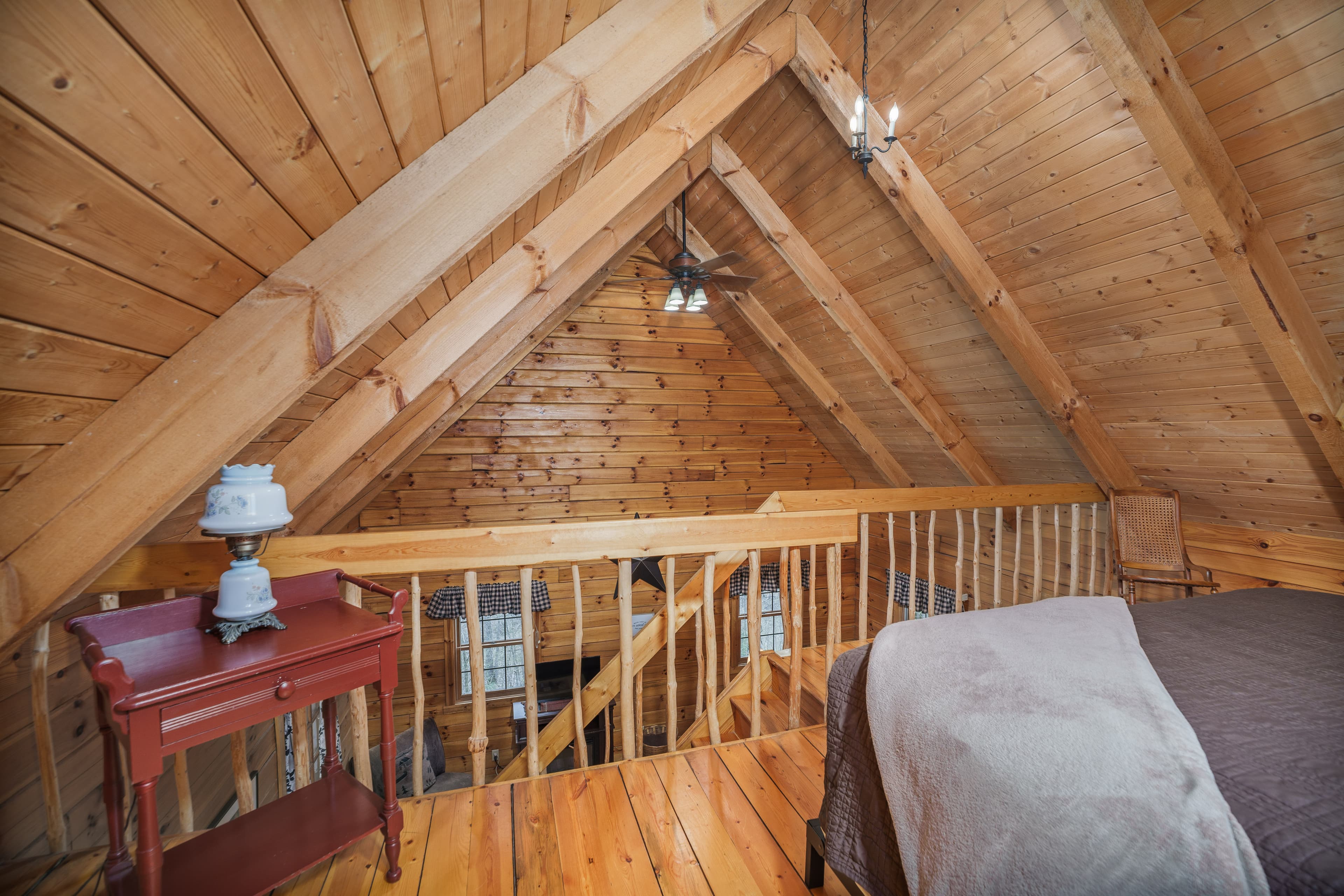 Cozy attic interior with wooden beams, a bed, a small table, and a view of the railing.