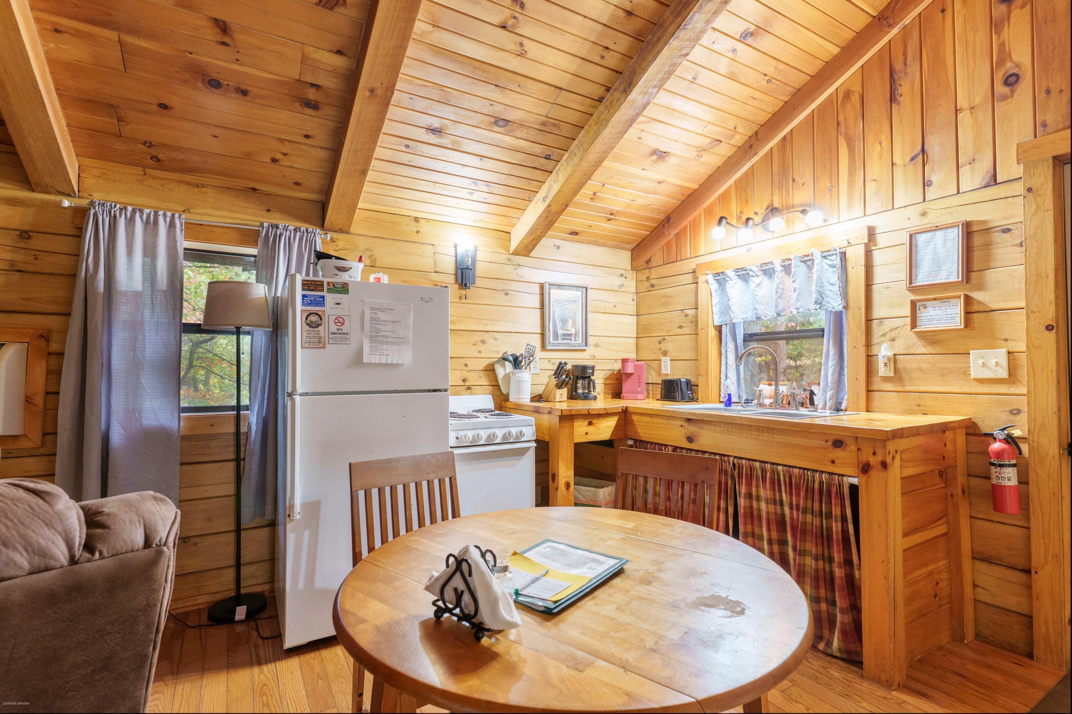 Cozy wooden cabin interior featuring a kitchen area, dining table, and natural light from windows.