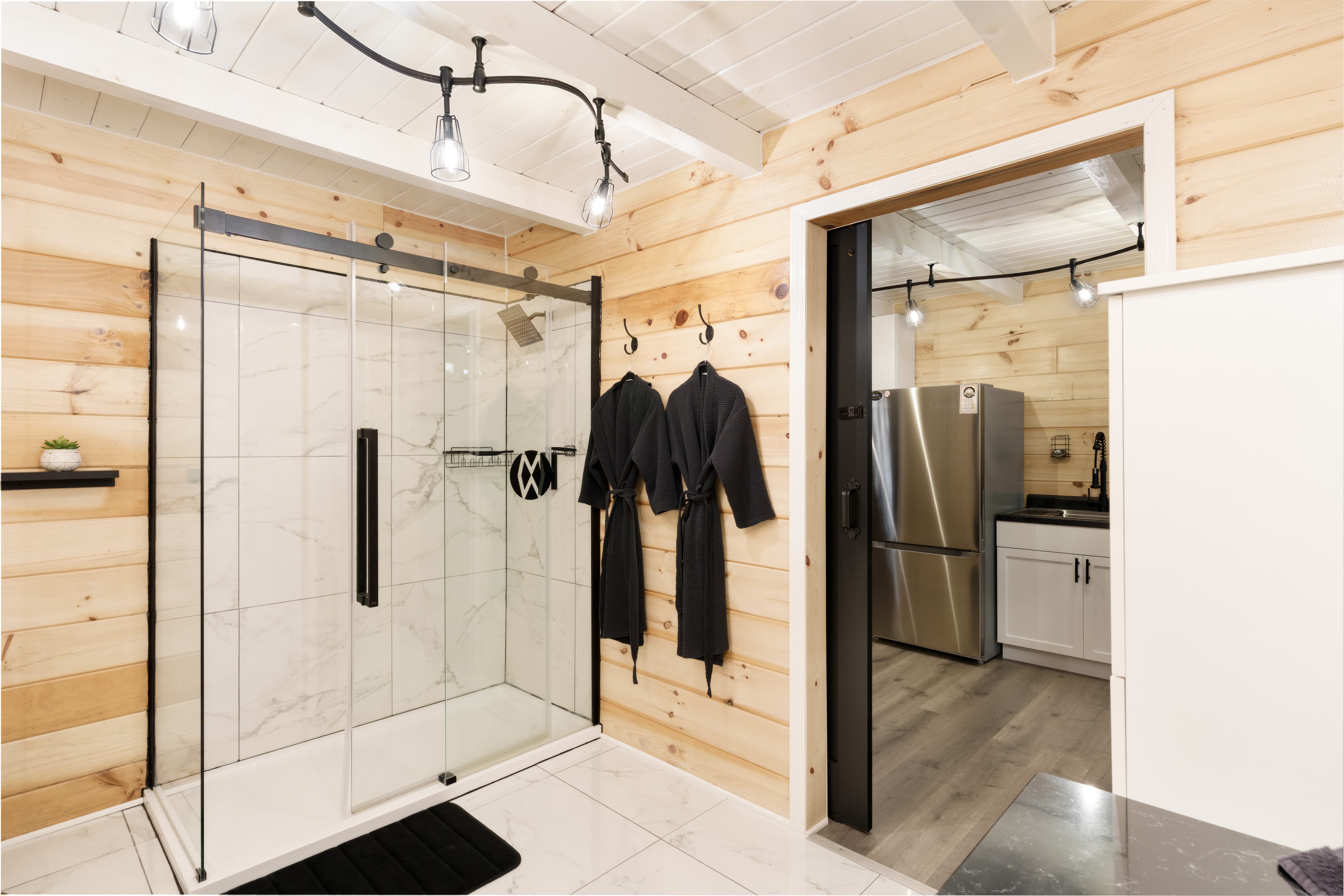 Modern bathroom featuring a glass shower, wooden walls, and black robes hanging by the door.