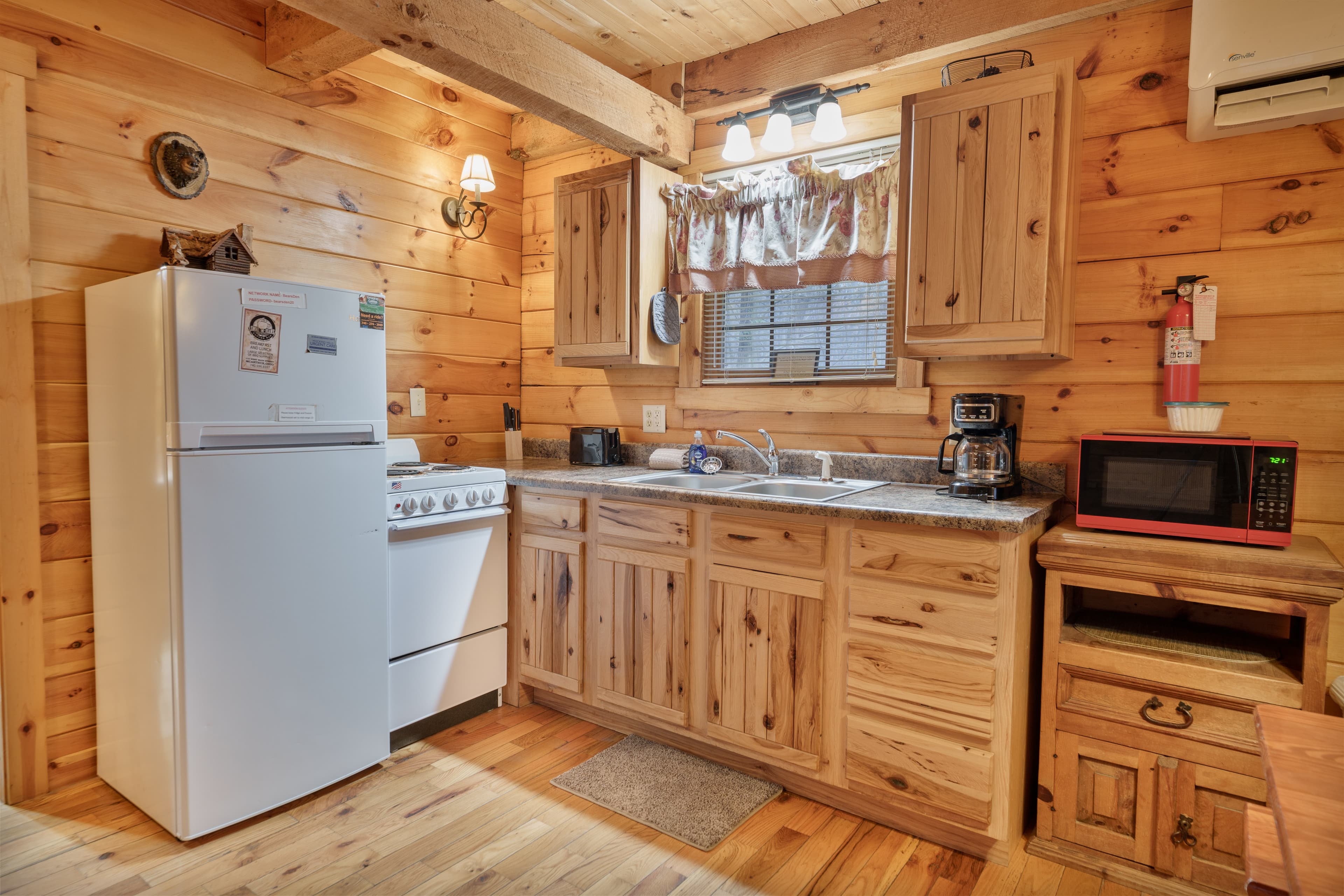 A cozy wooden kitchen featuring a white refrigerator, stove, sink, and microwave with rustic cabinetry.