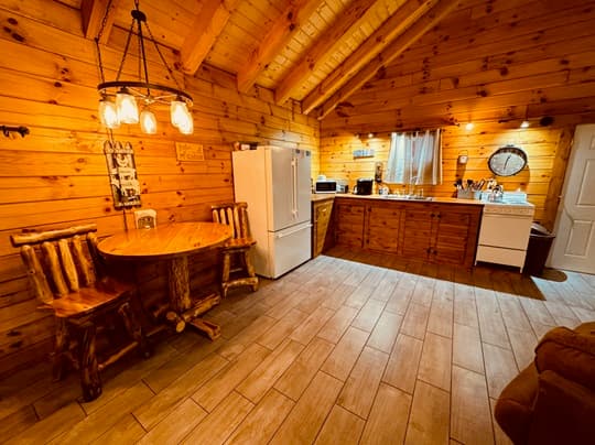 A rustic kitchen with wooden walls, a round table, and a refrigerator.