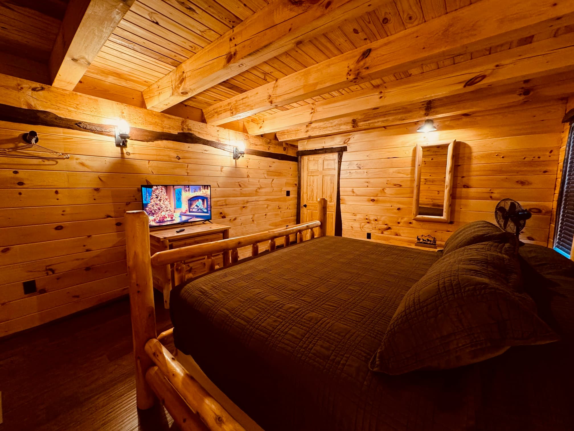 Cozy wooden bedroom with a log bed, TV, and warm lighting.