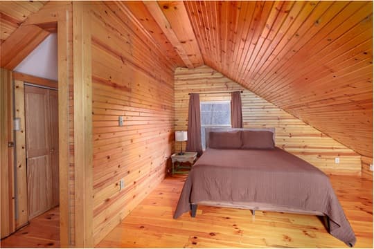 Cozy wood-paneled bedroom featuring a double bed, window with curtains, and a bedside lamp.
