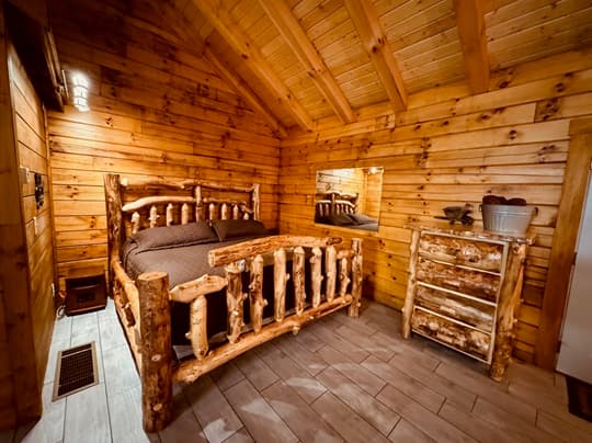 Cozy wooden cabin interior featuring a log bed, dresser, and warm lighting.