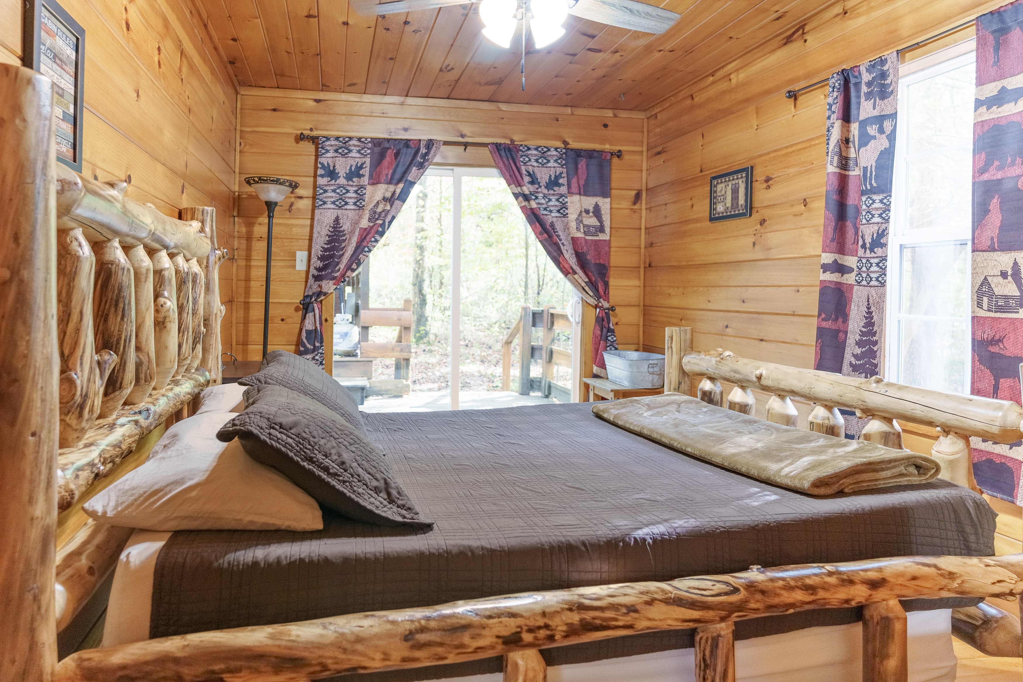 Cozy wooden bedroom featuring a log bed, patterned curtains, and a view of the outdoors.