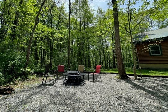 A fire pit area with four chairs surrounded by trees in a gravel clearing.